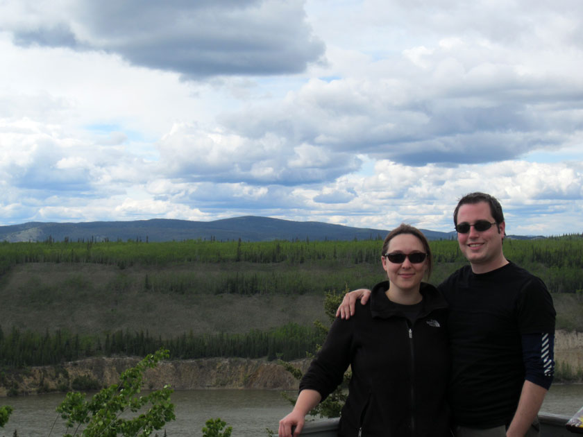 couple standing with a river and forest behind them