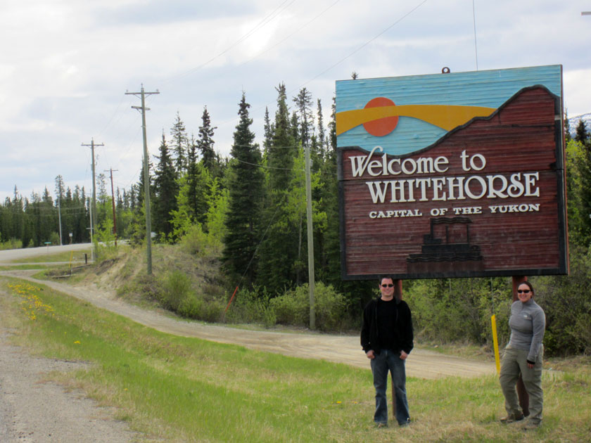 couple standing in front of a wooden sign that reads 'Welcome to Whitehorse capital of the Yukon'