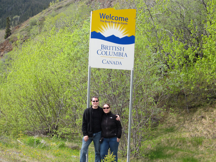 couple in front of a sign reading 'Welcome the best place on earth British Columbia, Canada