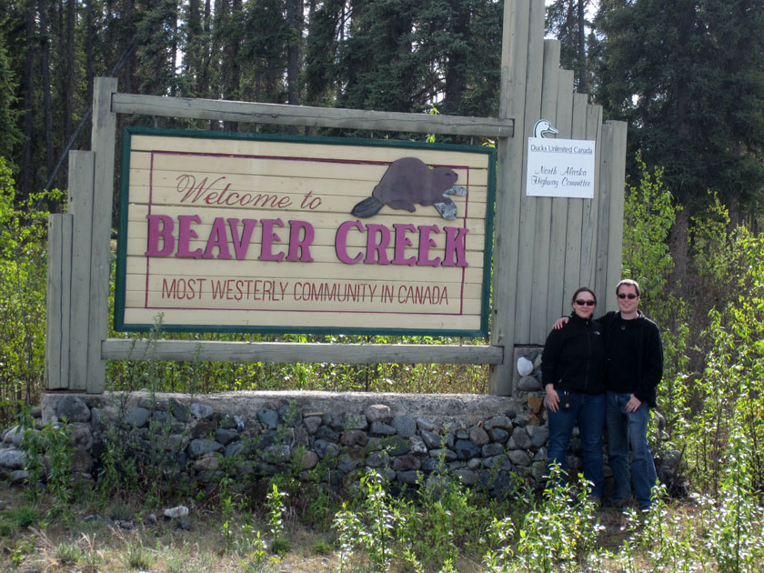 couple standing in front of a wooden sign reading 'Welcome to Beaver Creek most westerly community in Canada'