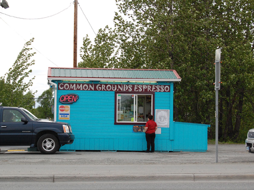 small shack with a sign reading 'common grounds espresso' and a woman ordering at the window