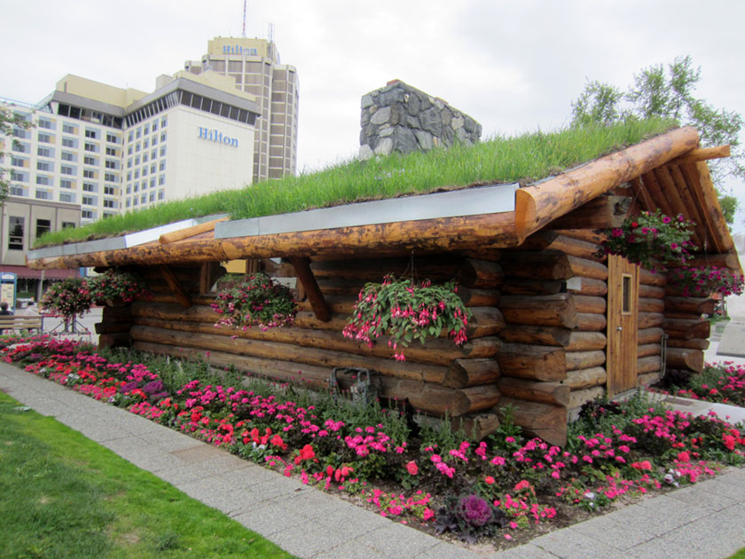 log cabin building with a grass roof and flowers all around it