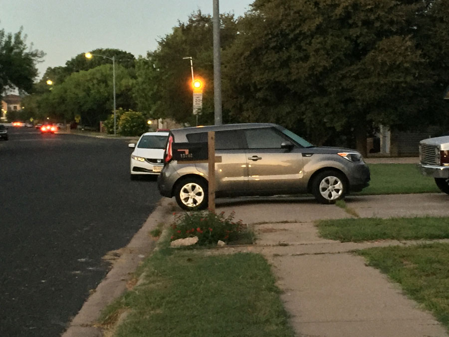 car parked over sidewalk near a flashing school zone sign