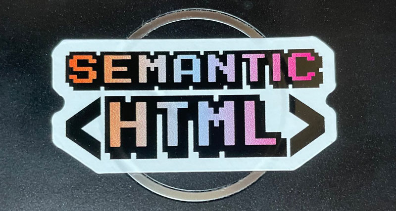 a color sticker about 2 inches wide cover a laptop logo. It says semantic HTML.